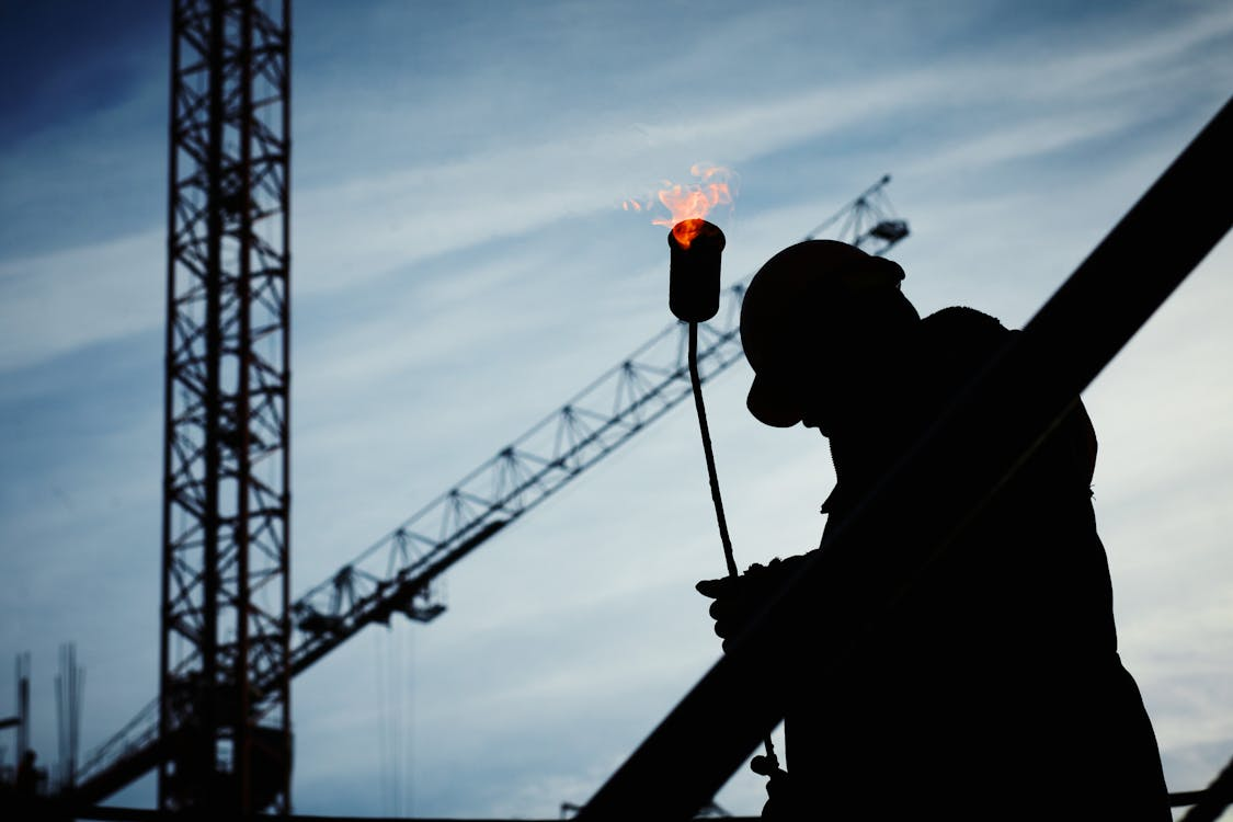 A construction worker holding a flamethrower near a construction site  