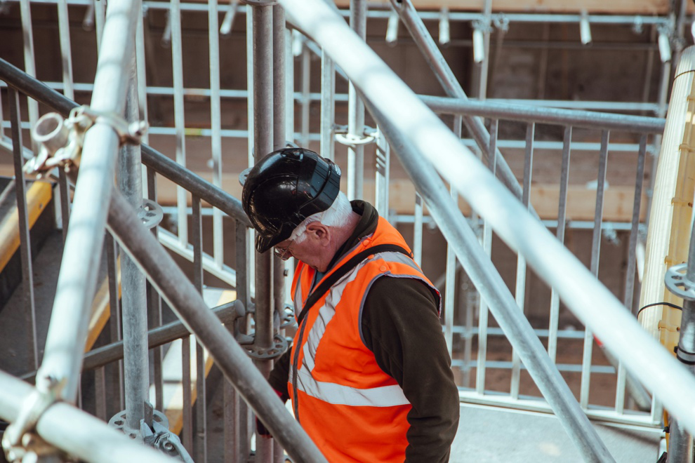 A man wearing a hard hat standing under scaffolding 