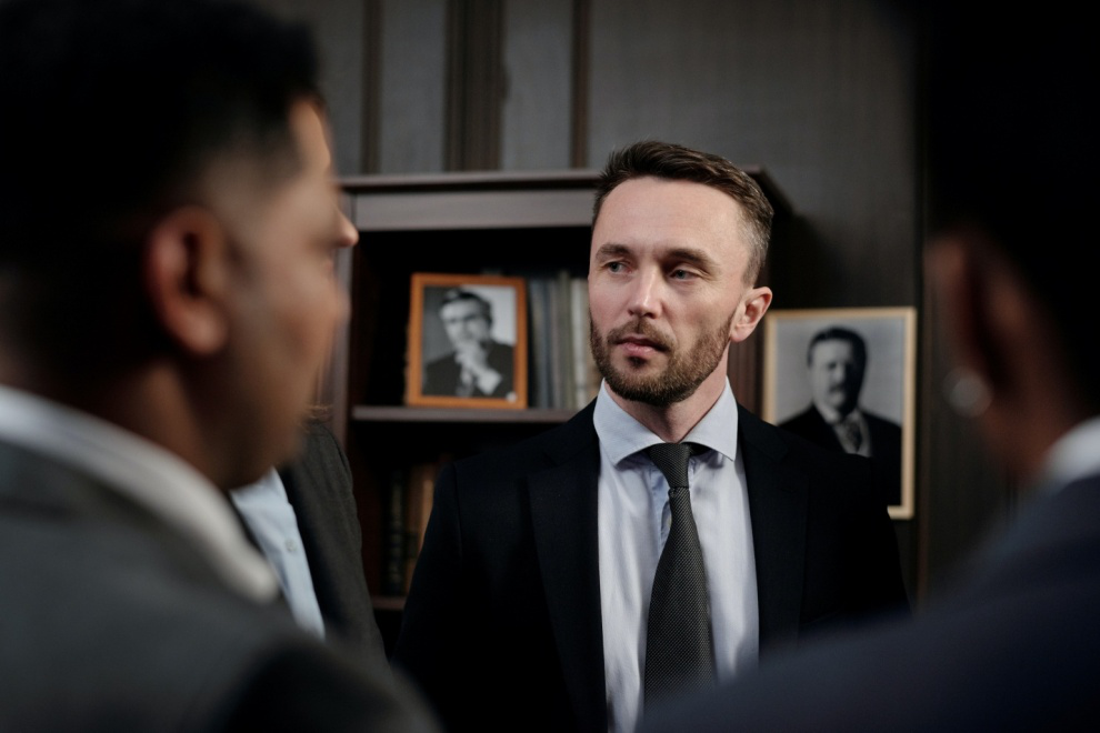 Two men in suits facing another in a black tie