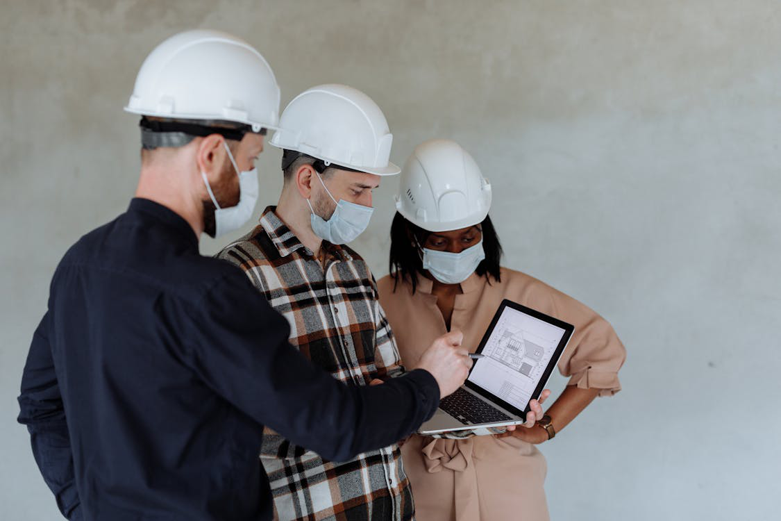  An image of three people wearing helmets and looking at a laptop 
