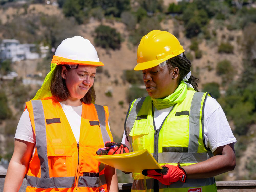 An image of two women wearing helmets and jackets while talking to each other   