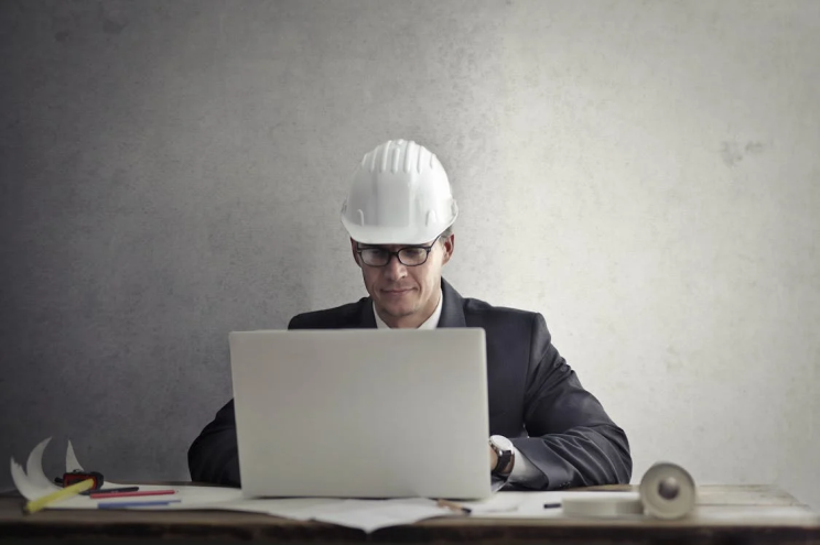 An image of a man wearing a white helmet and working on a laptop   