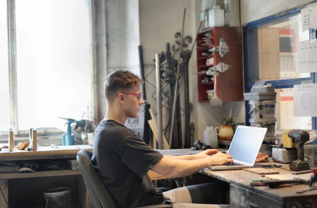 A focused man working on a laptop in a workshop.
