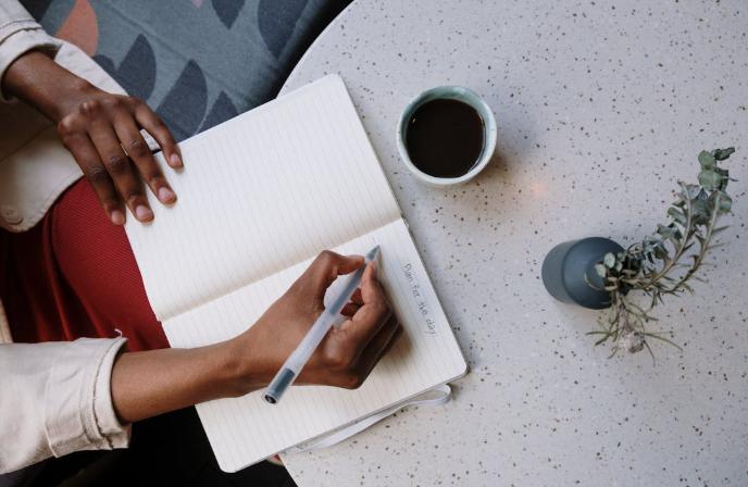 A person holding a white pen and writing on white paper.
