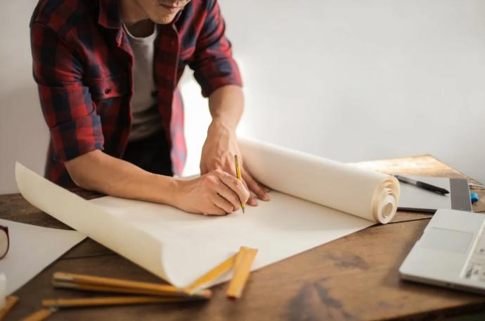  A male construction professional drawing plans on a paper roll.