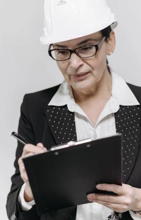 An elegant woman wearing a construction helmet and writing in a notepad.